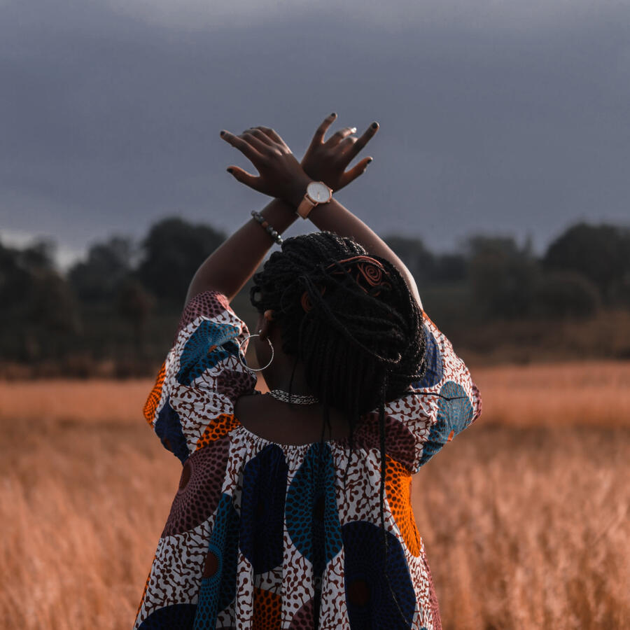 Black woman in the outdoors with arms raised and crossed at the wrists.